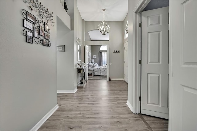 corridor with baseboards, wood finished floors, and an inviting chandelier