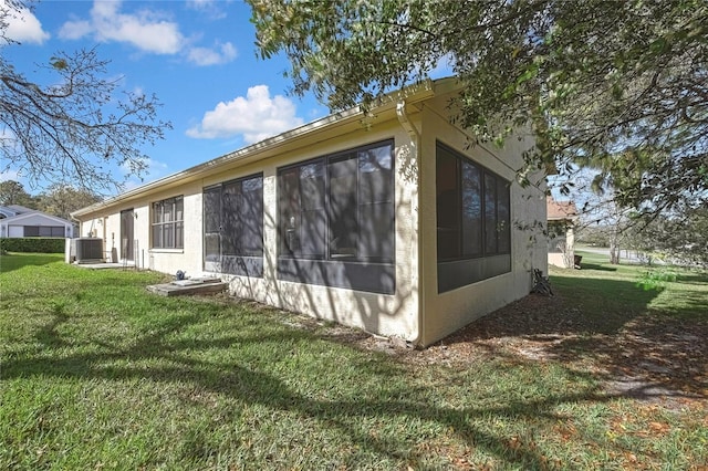 view of property exterior featuring a sunroom, central AC unit, stucco siding, and a yard