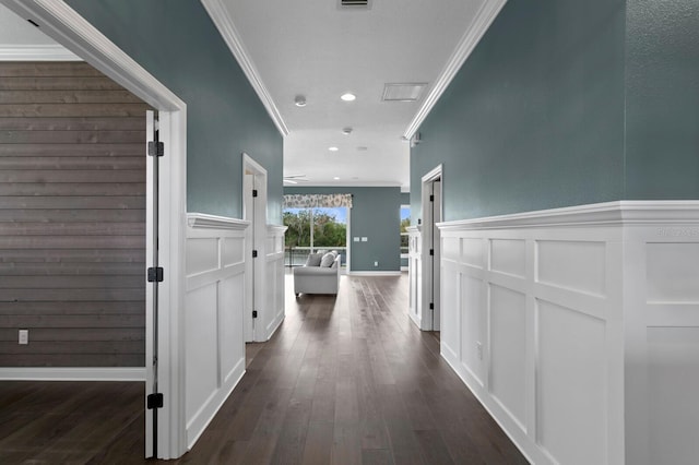 hall featuring a wainscoted wall, ornamental molding, dark wood-style flooring, and a decorative wall