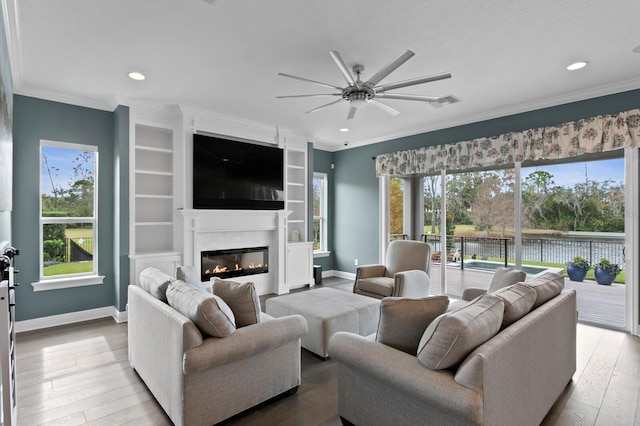 living room featuring baseboards, hardwood / wood-style floors, a glass covered fireplace, and crown molding