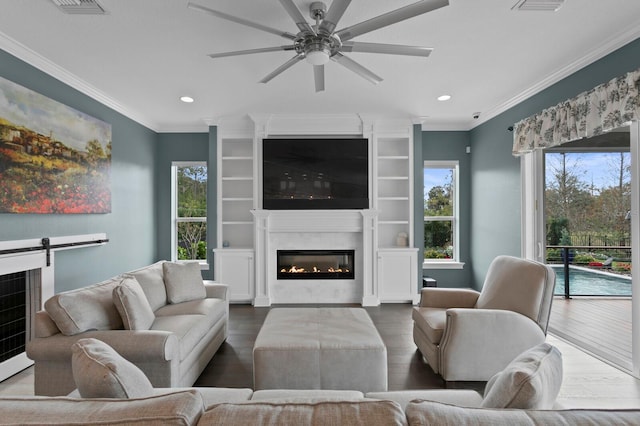 living area with wood finished floors, a glass covered fireplace, a ceiling fan, and crown molding