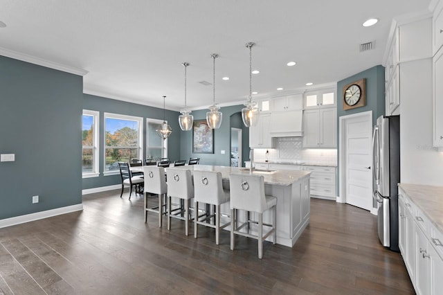 kitchen featuring an island with sink, dark wood finished floors, backsplash, and freestanding refrigerator