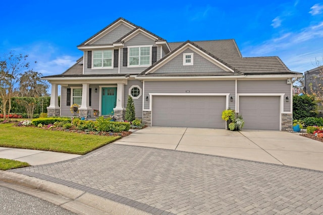 craftsman-style home featuring an attached garage, covered porch, stone siding, concrete driveway, and a front lawn