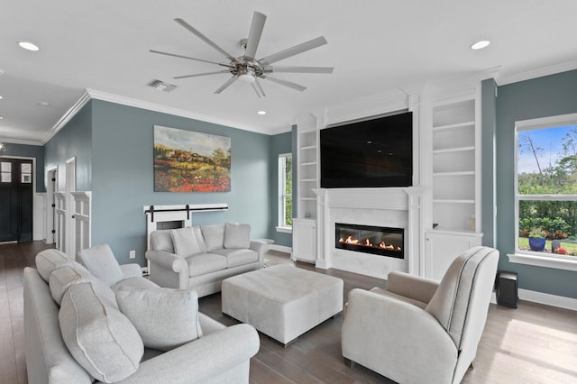 living room featuring a glass covered fireplace, wood finished floors, visible vents, and crown molding