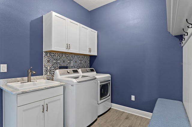 clothes washing area featuring cabinet space, light wood-style flooring, a sink, washer and dryer, and baseboards