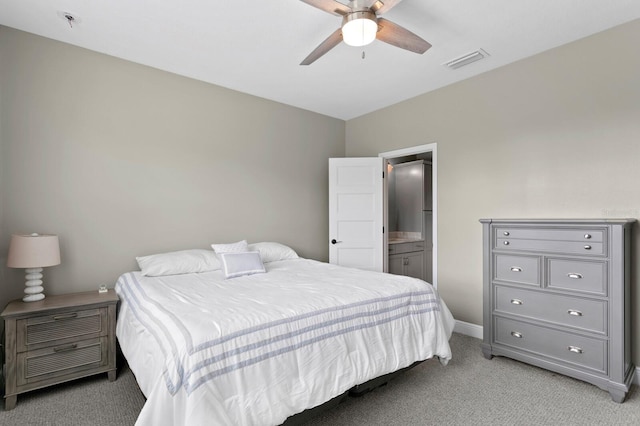 bedroom with ceiling fan, light colored carpet, visible vents, baseboards, and ensuite bath