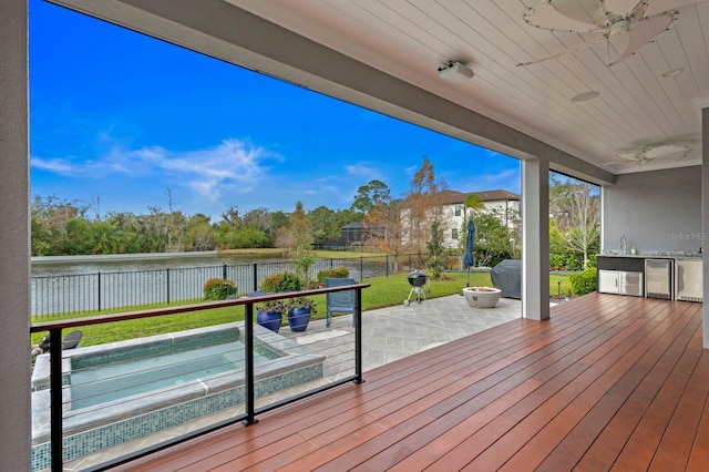 deck with a fenced backyard, a water view, a sink, a ceiling fan, and a lawn