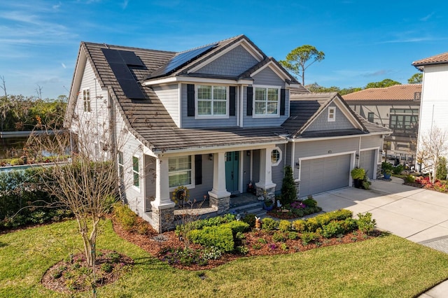 craftsman-style house featuring a porch, a garage, driveway, roof mounted solar panels, and a front yard