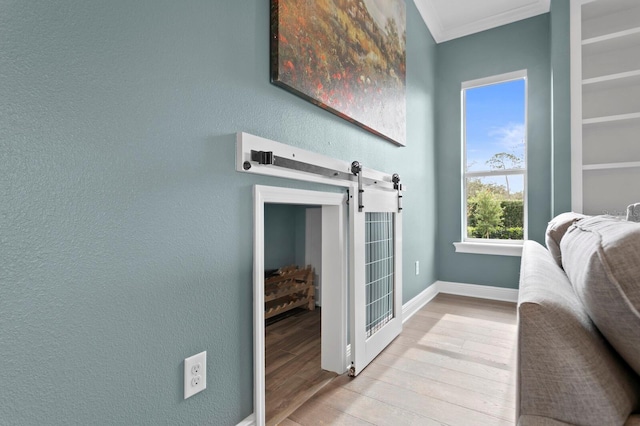 interior space with a barn door, baseboards, a textured wall, wood finished floors, and crown molding