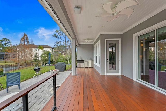 deck with a sink, ceiling fan, fence, and a lawn