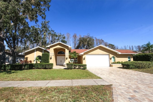 view of front of property with a garage, decorative driveway, a front lawn, and stucco siding