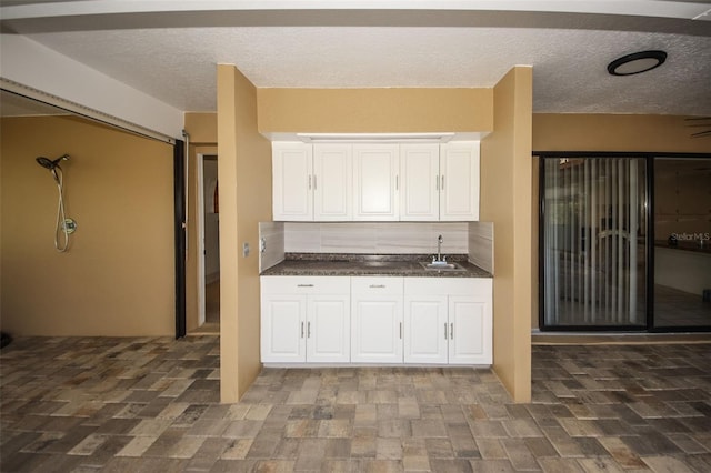 kitchen with a textured ceiling, dark countertops, a sink, and white cabinets