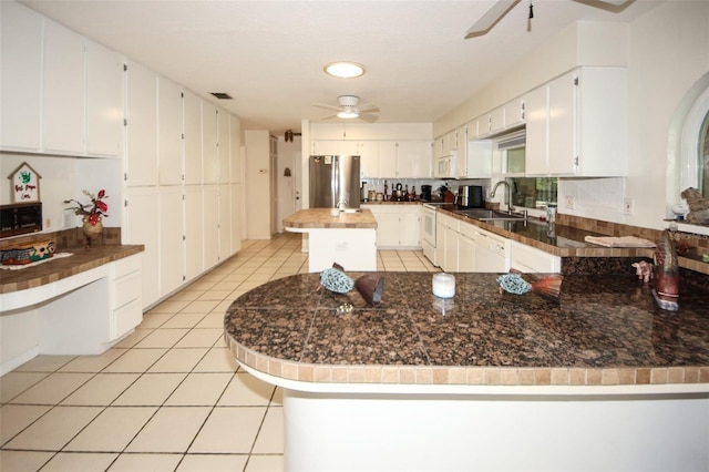 kitchen with light tile patterned floors, a ceiling fan, a sink, white appliances, and a peninsula