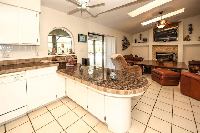 kitchen featuring light tile patterned floors, a peninsula, a fireplace, open floor plan, and dishwasher