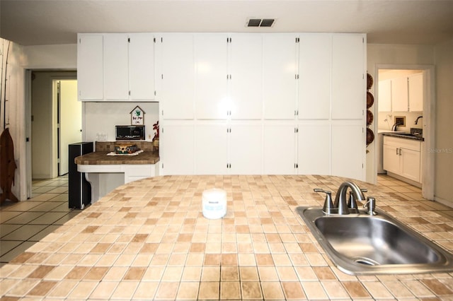 kitchen featuring tile countertops, visible vents, white cabinets, a sink, and tile patterned floors