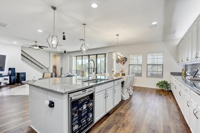 kitchen featuring arched walkways, dark wood finished floors, a center island with sink, a sink, and dishwasher