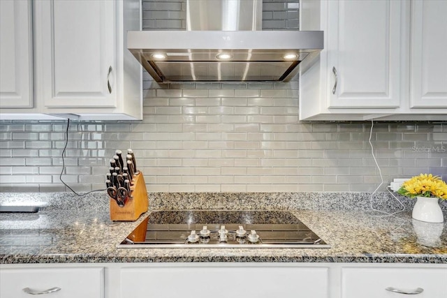 kitchen with stone counters, black electric cooktop, white cabinetry, wall chimney range hood, and tasteful backsplash