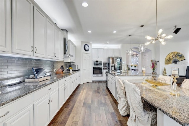 kitchen featuring stone countertops, decorative backsplash, stainless steel fridge with ice dispenser, dark wood-type flooring, and hanging light fixtures