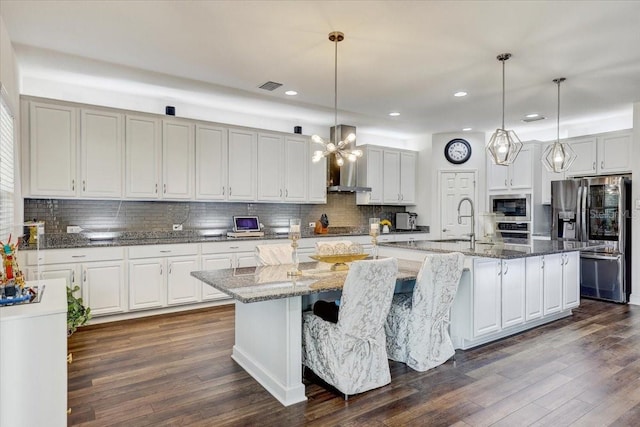 kitchen featuring dark wood-style floors, stainless steel appliances, a sink, a large island with sink, and wall chimney exhaust hood