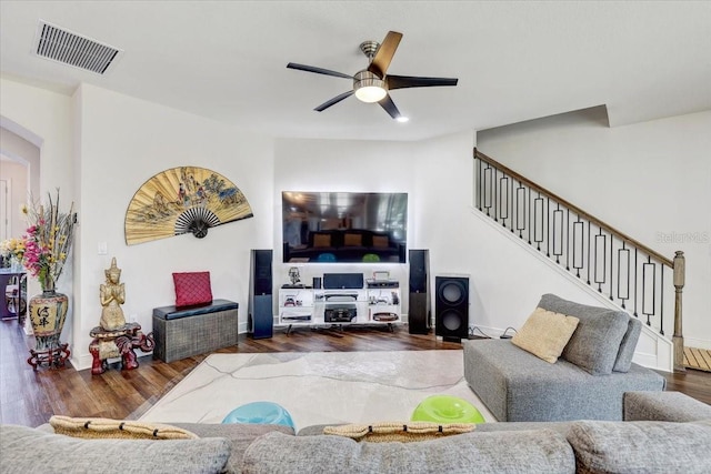 living room featuring baseboards, visible vents, a ceiling fan, wood finished floors, and stairs