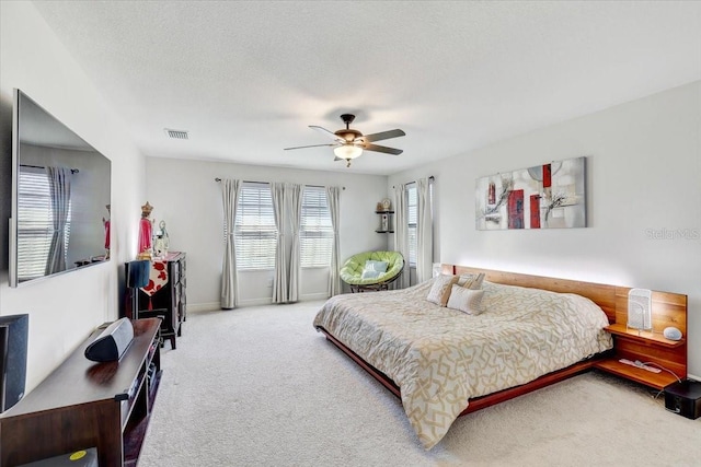 carpeted bedroom featuring baseboards, ceiling fan, visible vents, and a textured ceiling