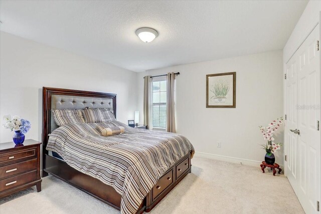 bedroom featuring light carpet, a textured ceiling, and baseboards