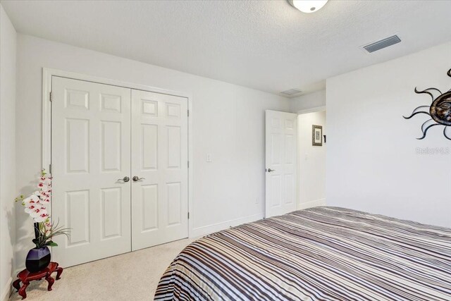 carpeted bedroom with a textured ceiling, visible vents, and a closet