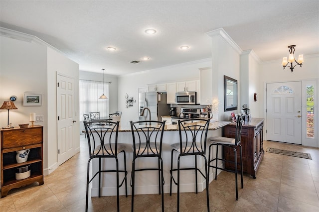 kitchen with light stone countertops, appliances with stainless steel finishes, a peninsula, a kitchen breakfast bar, and white cabinets