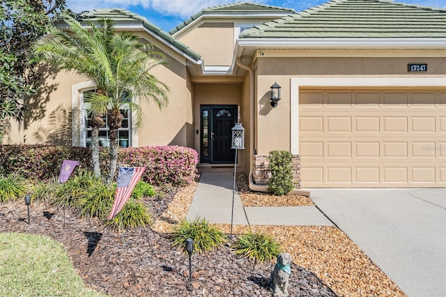 view of exterior entry featuring stucco siding, a garage, concrete driveway, and a tiled roof