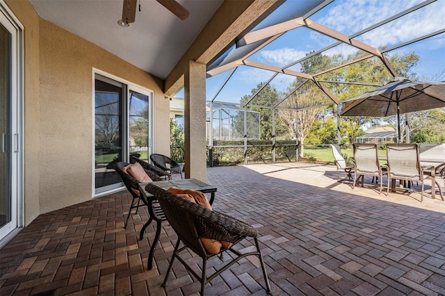 view of patio featuring glass enclosure, outdoor dining area, and a ceiling fan