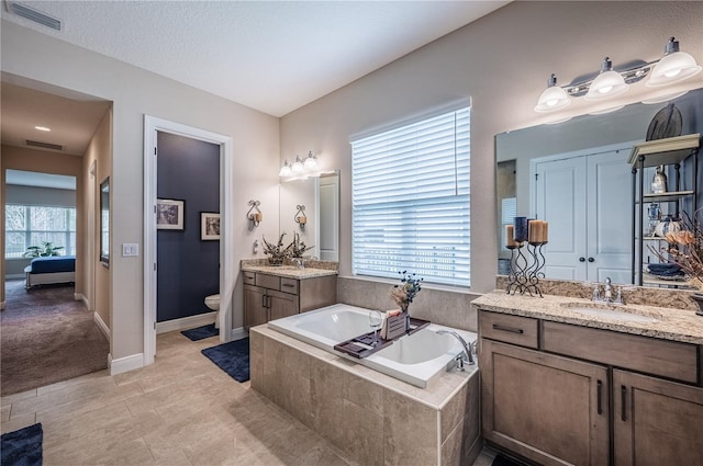 ensuite bathroom featuring a bath, a sink, a healthy amount of sunlight, and visible vents