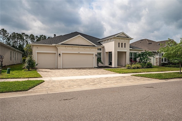 view of front of property with a shingled roof, decorative driveway, a front yard, an attached garage, and stucco siding