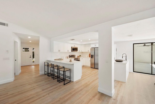 kitchen with light wood-style flooring, a peninsula, a breakfast bar, visible vents, and appliances with stainless steel finishes