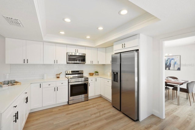 kitchen with stainless steel appliances, a raised ceiling, visible vents, and light wood-style flooring