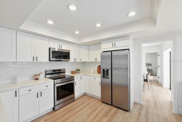 kitchen featuring ornamental molding, stainless steel appliances, light countertops, and a raised ceiling