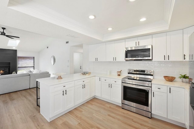 kitchen featuring appliances with stainless steel finishes, a raised ceiling, a large fireplace, and a peninsula