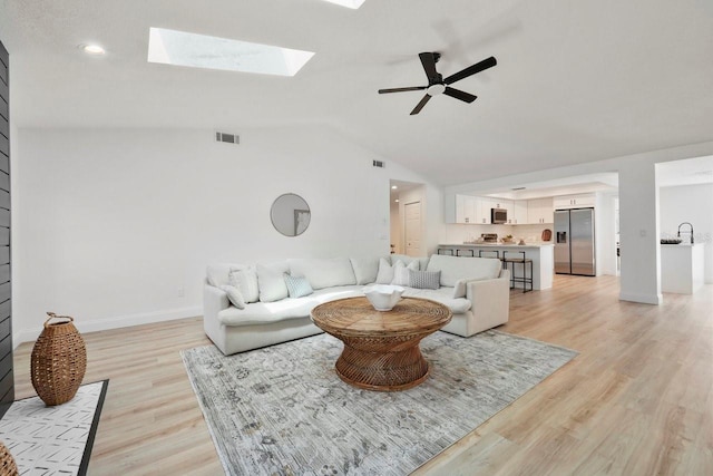 living room with visible vents, baseboards, lofted ceiling with skylight, ceiling fan, and light wood-type flooring