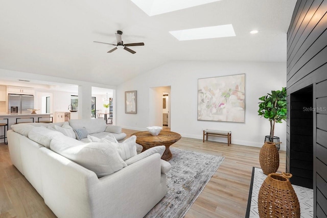 living area featuring vaulted ceiling with skylight, baseboards, a ceiling fan, light wood-style flooring, and recessed lighting