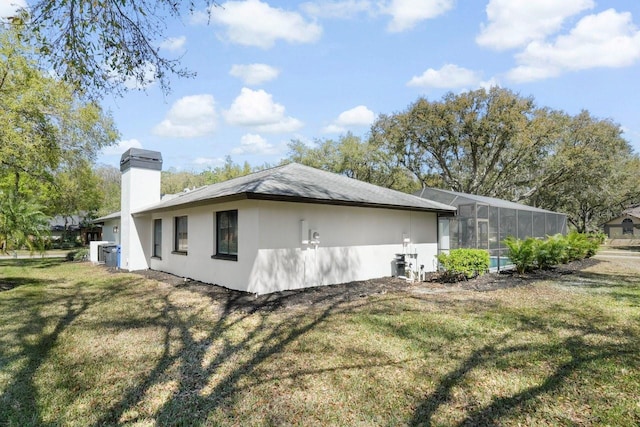 view of side of property with a lanai, stucco siding, a chimney, and a yard