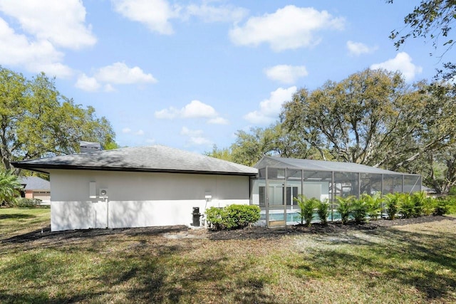 back of house featuring a lawn, stucco siding, a lanai, and an outdoor pool