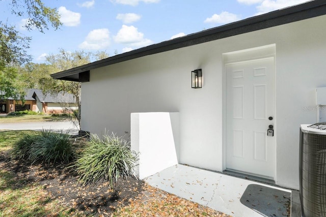 doorway to property with central AC unit and stucco siding