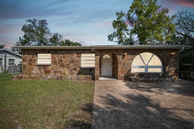 view of front of house featuring stone siding, a yard, and fence