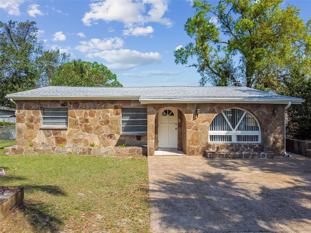 view of front of property with stone siding, a front lawn, and roof with shingles