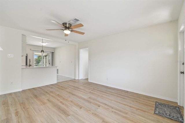 unfurnished living room with visible vents, baseboards, ceiling fan, light wood-type flooring, and a sink