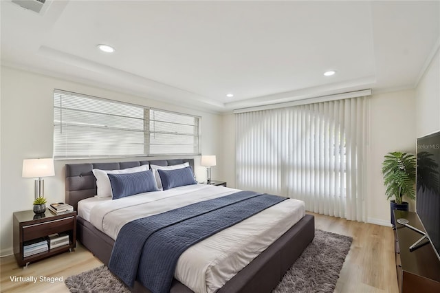 bedroom featuring a raised ceiling, multiple windows, light wood-style floors, and visible vents