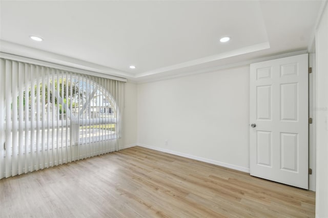 spare room with a raised ceiling, recessed lighting, light wood-type flooring, and baseboards