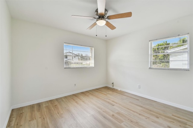 empty room featuring a wealth of natural light, baseboards, light wood-style floors, and a ceiling fan