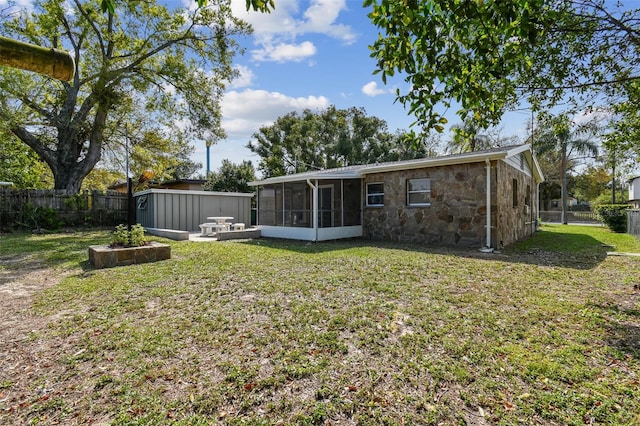 back of property with an outdoor structure, a fenced backyard, a lawn, and a sunroom