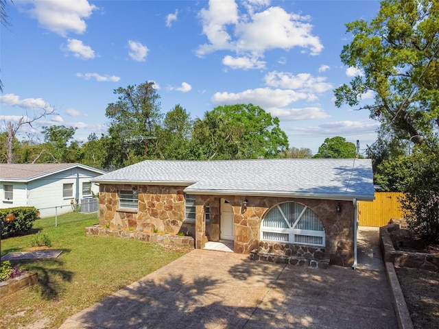 view of front of property featuring a front lawn, fence, stone siding, and a shingled roof