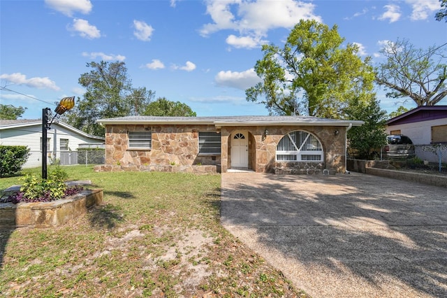 view of front facade with stone siding, driveway, a front lawn, and fence